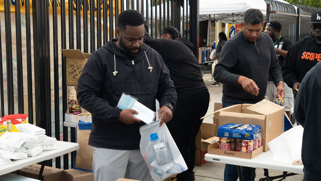 People organizing food items on tables outdoors, with boxes and packages of supplies.